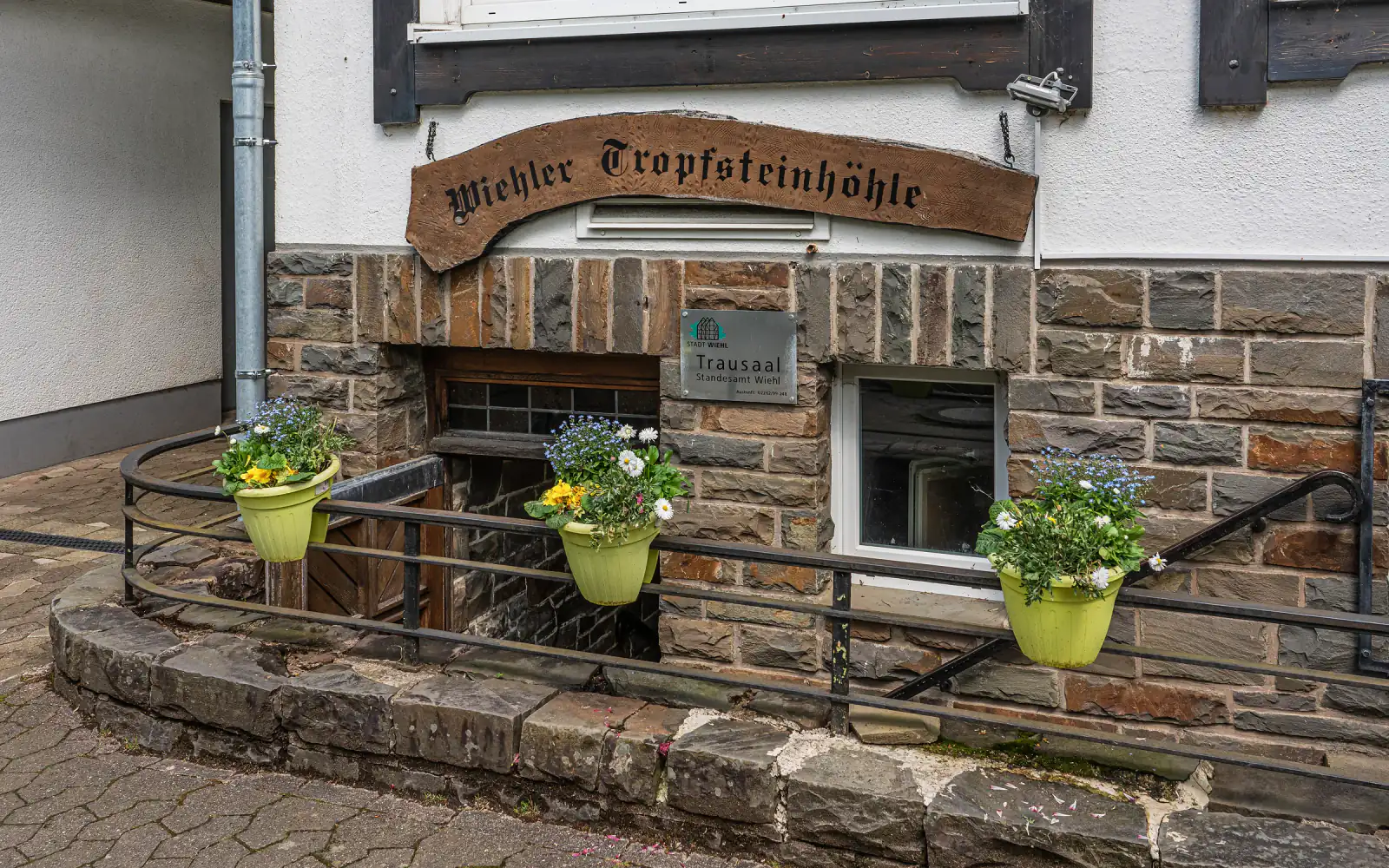 Eingang zur Wiehler Tropfsteinhöhle mit Holzschild und Blumenkübeln