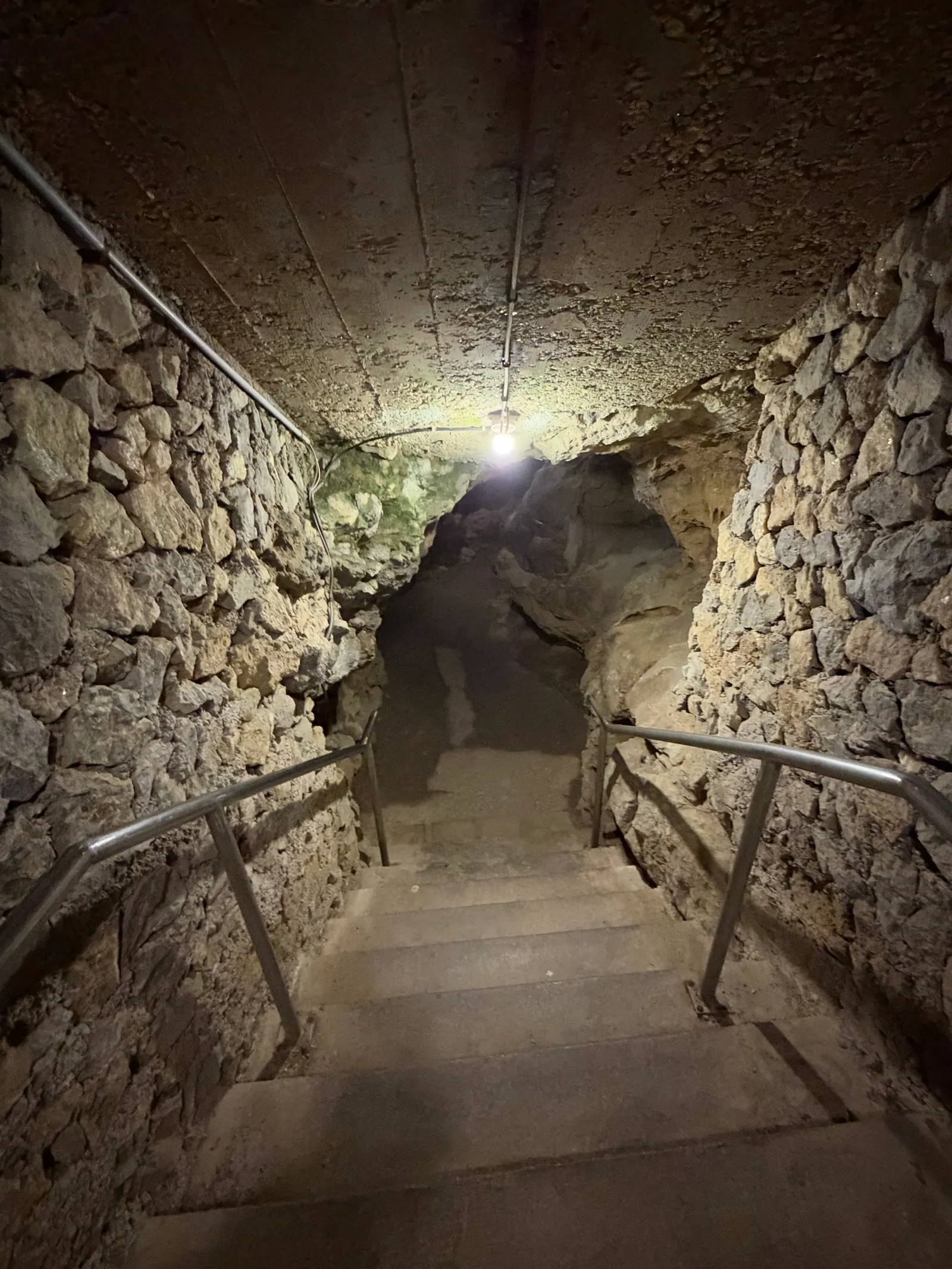 Treppe mit Geländer führt zwischen Steinmauern in den beleuchteten Stollen nach unten