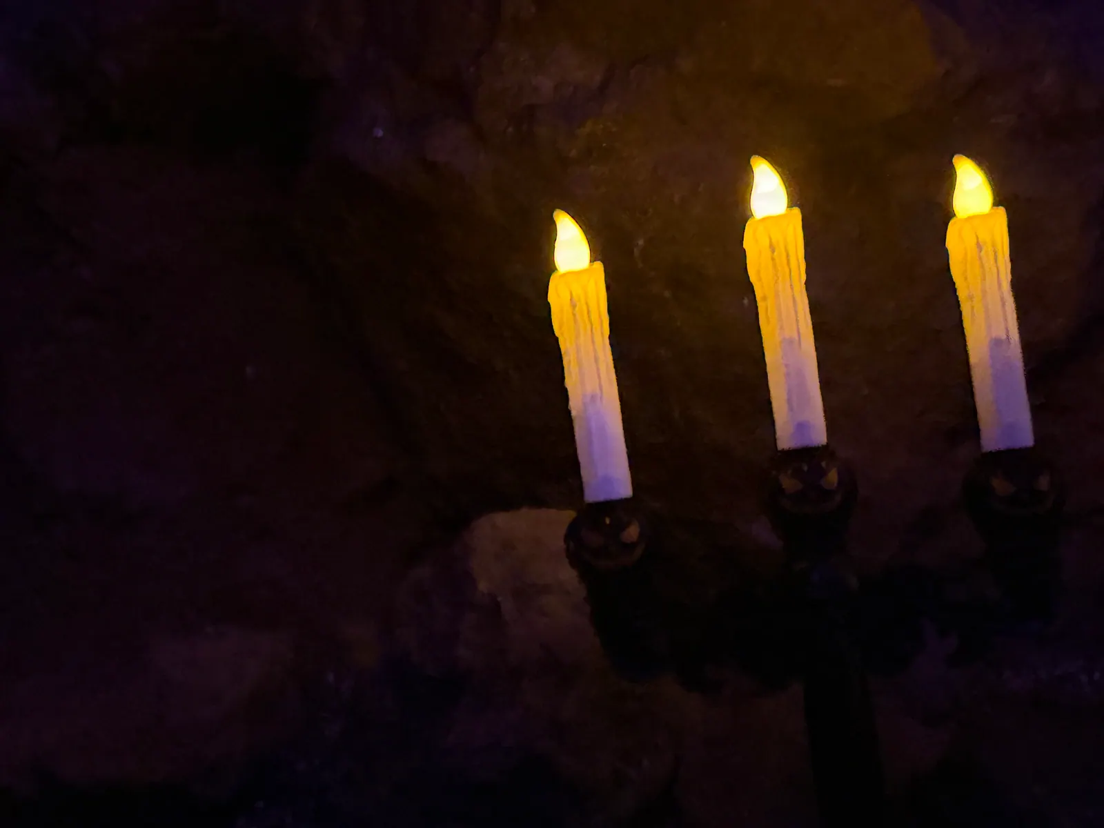 Schwarzer Kerzenleuchter mit drei brennenden Kerzen in der dunklen Höhle