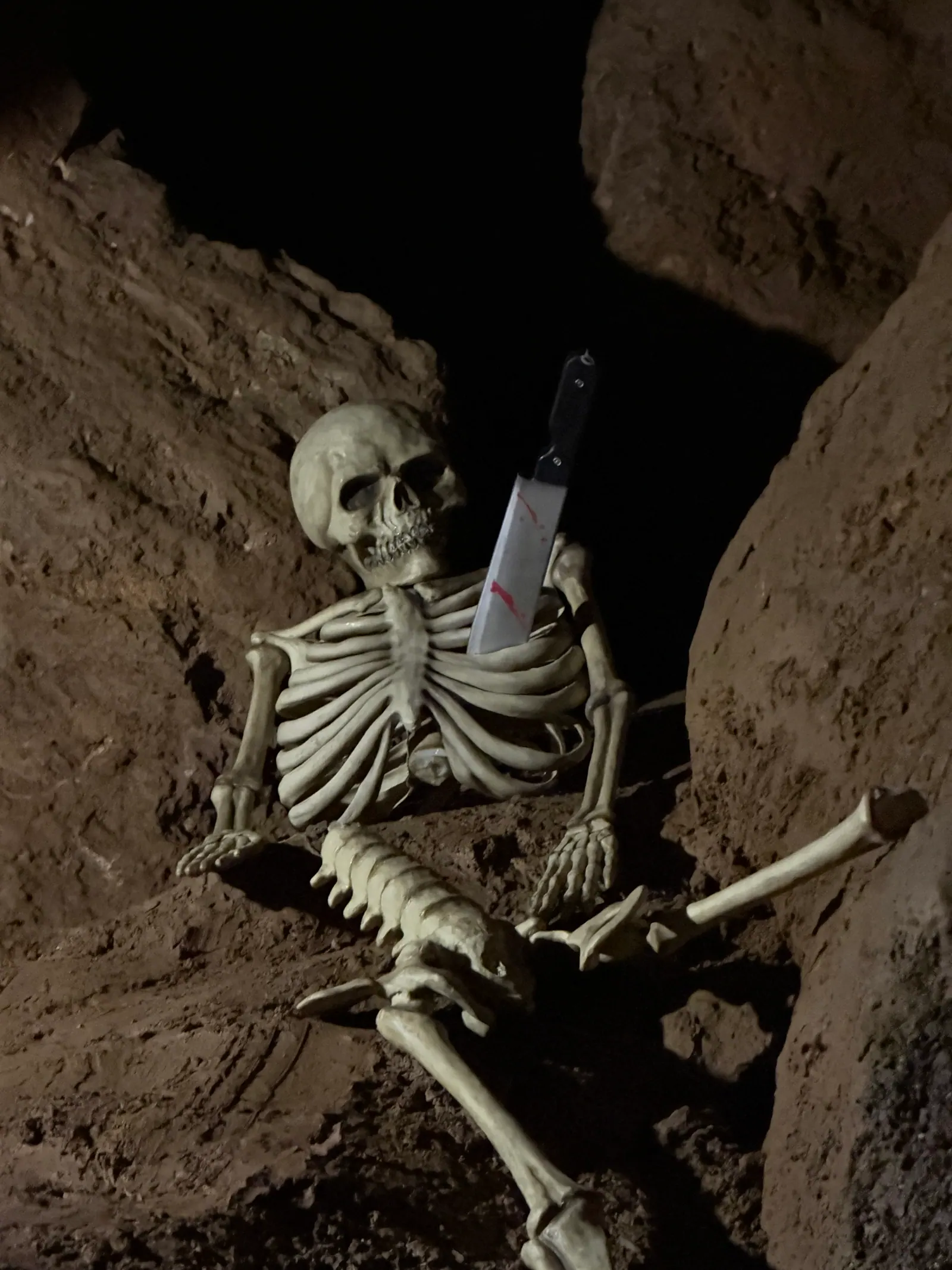 Skelett mit Messer sitzt zwischen Felsen in der Höhle