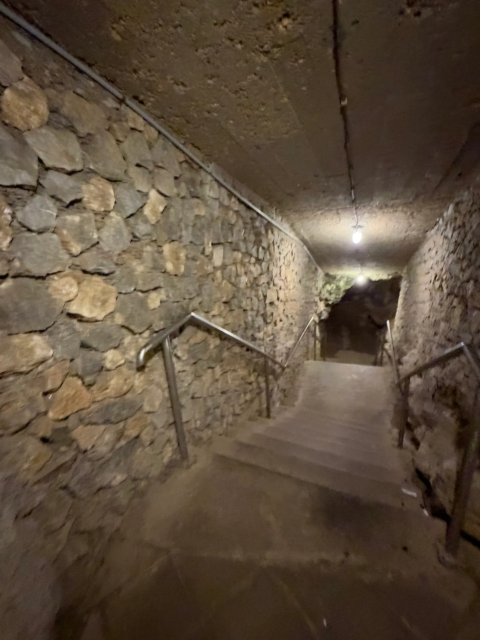 Treppe führt zwischen Bruchsteinmauern nach unten in die Höhle